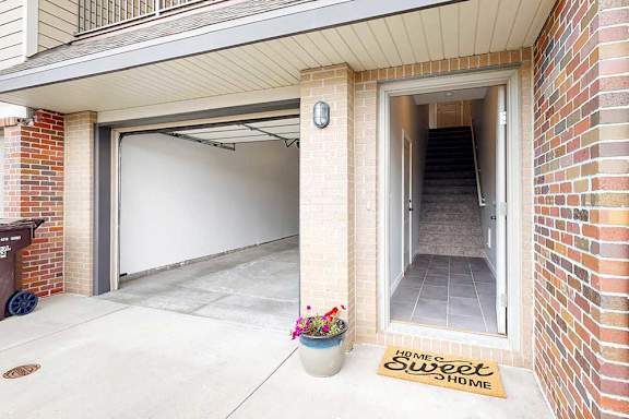 An apartment front door open to a staircase, next to an open garage door.