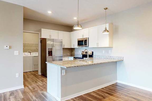 A kitchen with white wooden cabinets, granite countertops, stainless steel appliances, and a peninsula countertop.