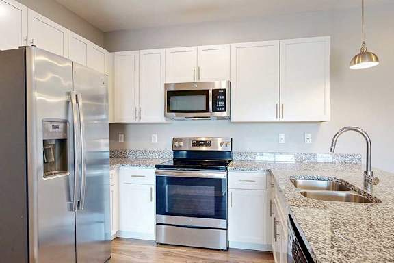 A kitchen with white wooden cabinets, granite countertops, and stainless steel appliances.