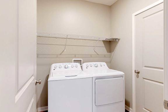 A full-sized washer and dryer in a laundry room, with overhead shelving.