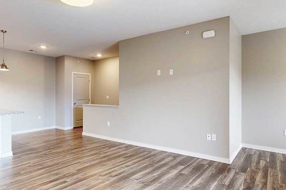 A living room with hardwood-style flooring, and a half-wall separating the stairway.