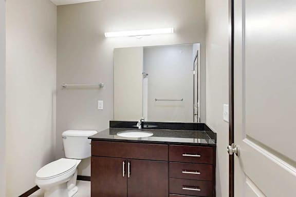 A bathroom with a granite vanity, dark wooden cabinets, and an oversized mirror with overhead lighting.