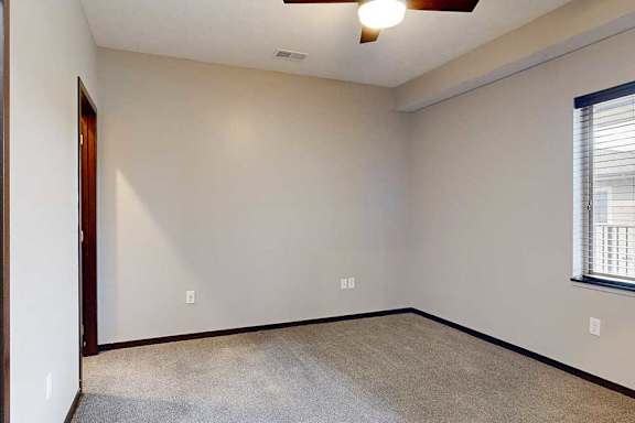A carpeted bedroom with a ceiling fan and a window.