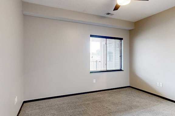 A carpeted bedroom with a ceiling fan and a window.