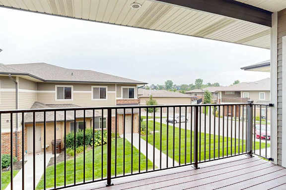 A spacious balcony with a black metal railing and a view of the neighborhood.