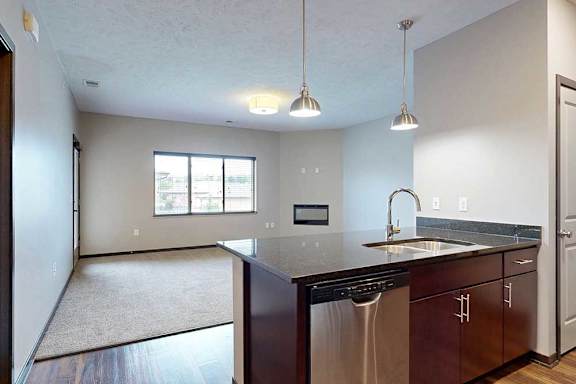 A kitchen peninsula with a double basin sink in front of a carpeted living room.