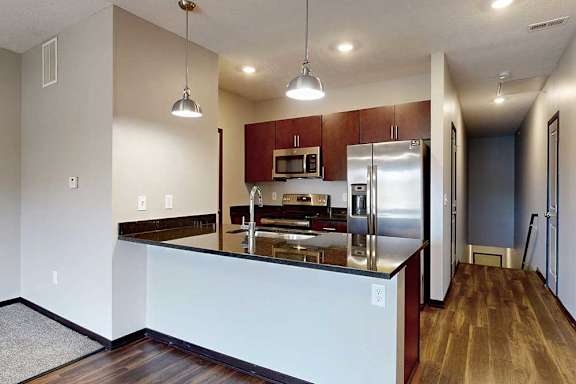 A galley kitchen with dark granite countertops, dark wooden cabinets, and stainless steel appliances.