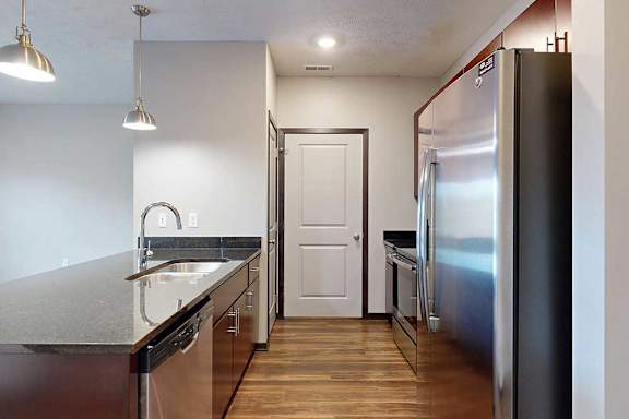 A galley kitchen with dark granite countertops, dark wooden cabinets, and stainless steel appliances.