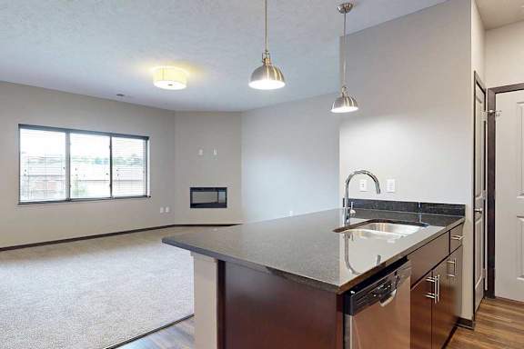 A kitchen peninsula with a double basin sink in front of a carpeted living room.