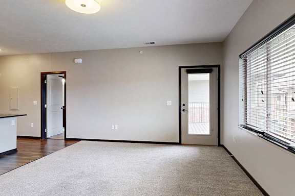 A carpeted living room with a large window and a windowed-door to the balcony.