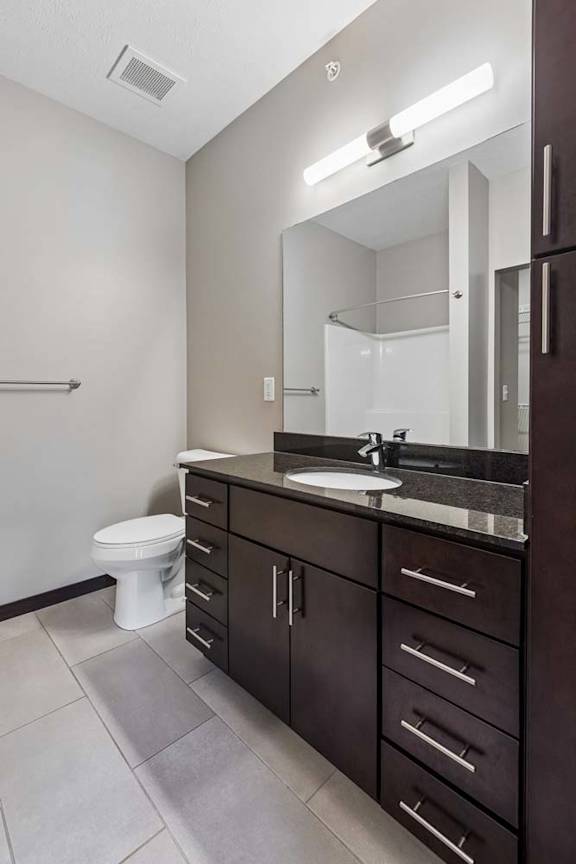 Apartment bathroom featuring a dark wood vanity, large mirror, and bright neutral finishes.