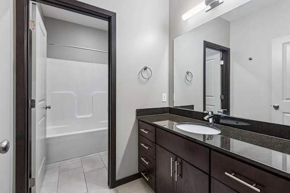 Bathroom with dark wood vanity, solid-surface countertop, framed mirror, and tub-shower combination.