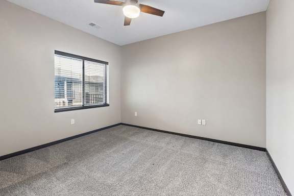 Spacious bedroom with large window, gray carpet, ceiling fan, and neutral finishes throughout.