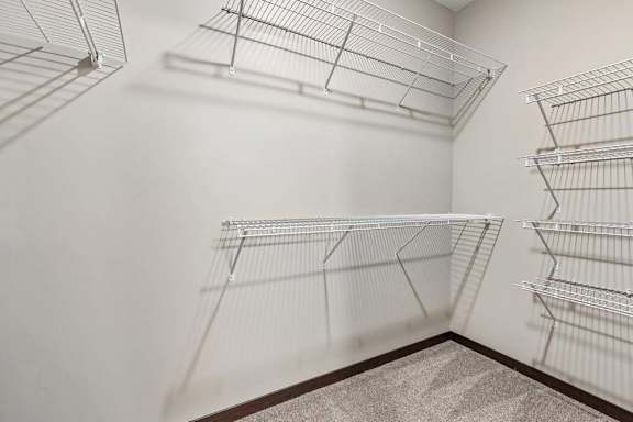 Walk-in closet with wire shelving, carpet flooring, and ample storage space for apartment living.