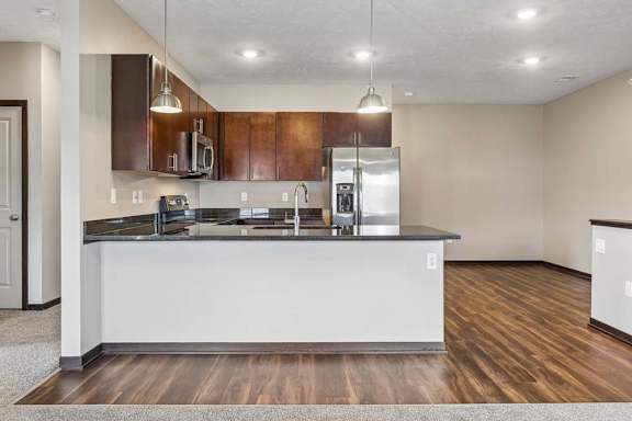 Modern kitchen with dark wood cabinetry, stainless steel appliances, peninsula seating, and wood-look flooring.