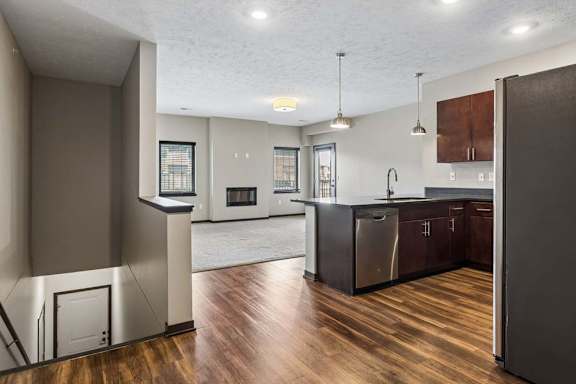 Open-concept apartment kitchen and living area with wood-look flooring, pendant lighting, and abundant natural light.