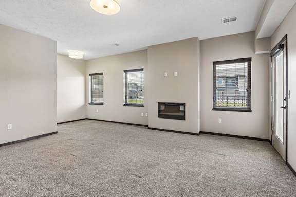 Open living room with corner fireplace, multiple windows, and neutral finishes in an apartment home.