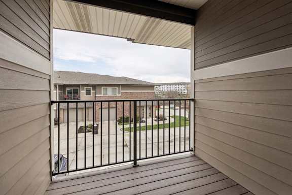 A balcony with a black railing and a view of a building and a cloudy sky.
