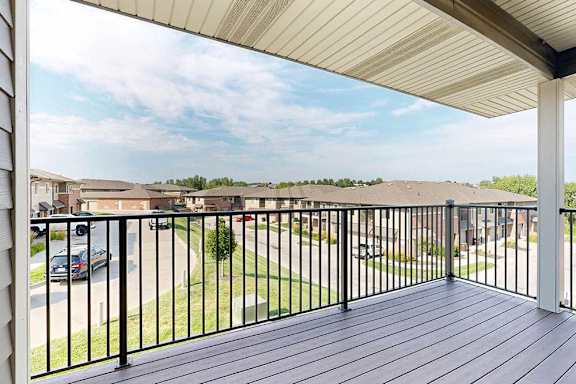 A spacious balcony with a black metal railing and a view of the neighborhood.