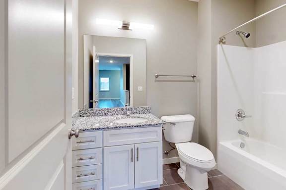 A bathroom with a granite vanity, white wooden cabinets, and a tub shower.