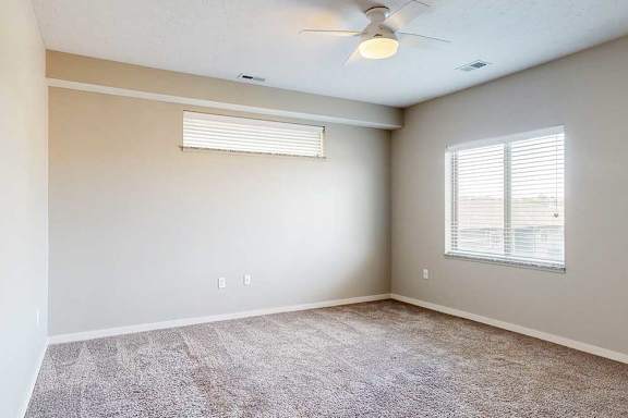 A carpeted bedroom with a ceiling fan, a large window, and an overhead half-window.
