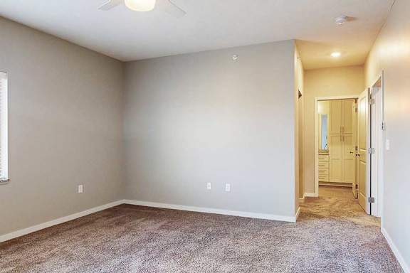A carpeted bedroom with a ceiling fan, and an ensuite bathroom and walk-in closet.