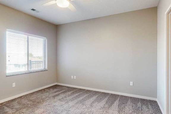 A carpeted bedroom with a large window and a ceiling fan.
