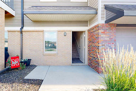 A brick apartment building with an open door to an apartment, and a patio space.