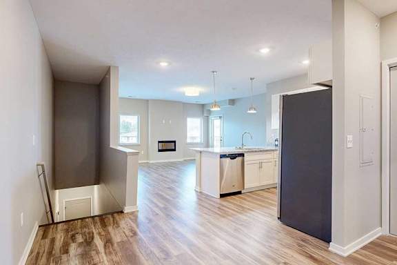 An entryway staircase leading up from the front door to an open living room and kitchen area with hardwood-style flooring.