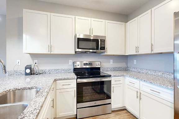 A kitchen with white wooden cabinets, granite countertops, stainless steel appliances, and a peninsula countertop.