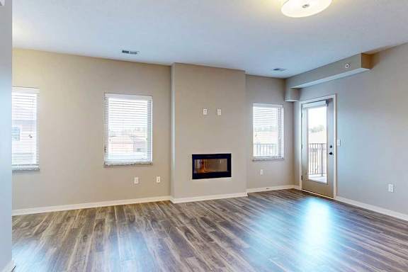 A living room with hardwood-style flooring, large windows, an electric fireplace, and a windowed door to a balcony.