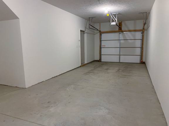 A large empty garage with a white door and a white ceiling light.