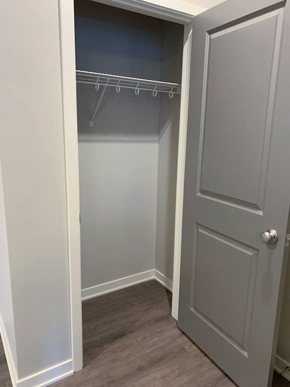 A white closet with a grey door and a grey shelf.