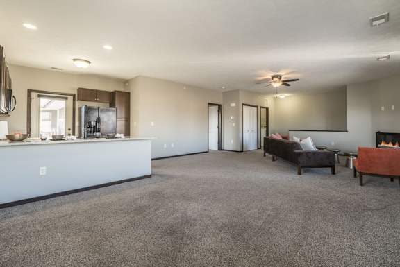 A spacious living room with a grey carpet and a kitchen area in the background.