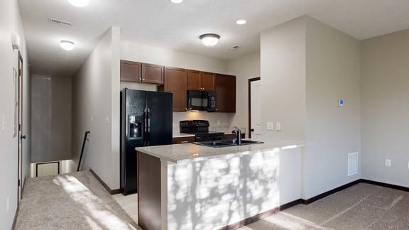 a galley kitchen with a granite countertop, dark wooden cabinets, and black appliances