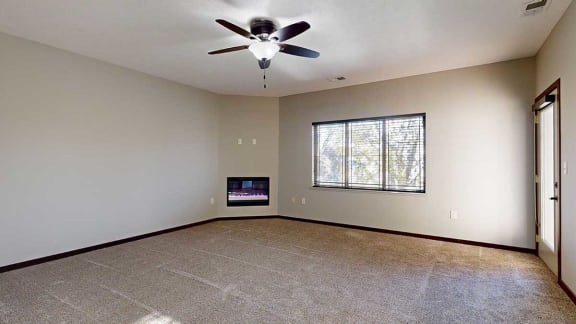 a carpeted living room with a ceiling fan, a fireplace, a large window, and a door to the balcony