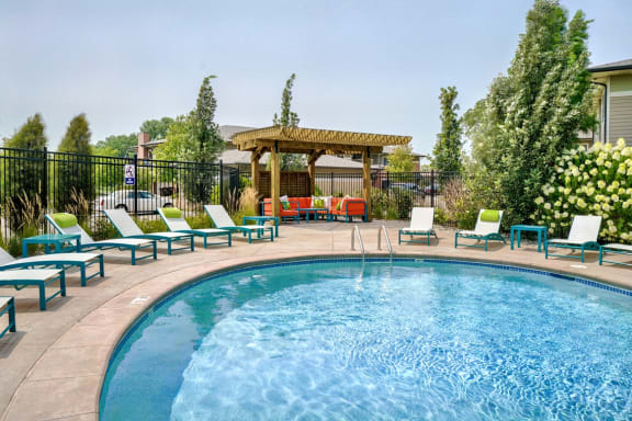Edge of blue pool with lounge chairs around it and wood pergola in the background