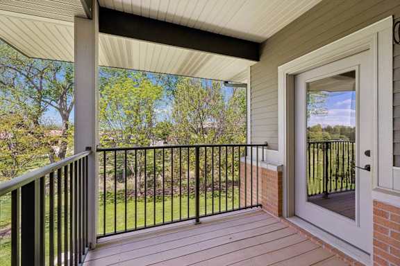 Private apartment balcony with black railing, wood-look decking, and a leafy green courtyard view.