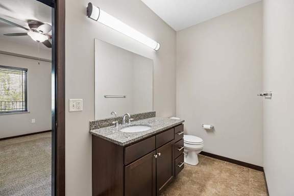 A bathroom with a sink, mirror, toilet and a fan.