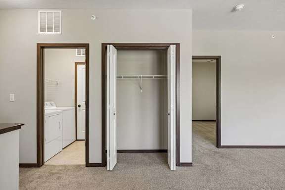 A room with a white wall and a carpeted floor with a white closet and a white washing machine.