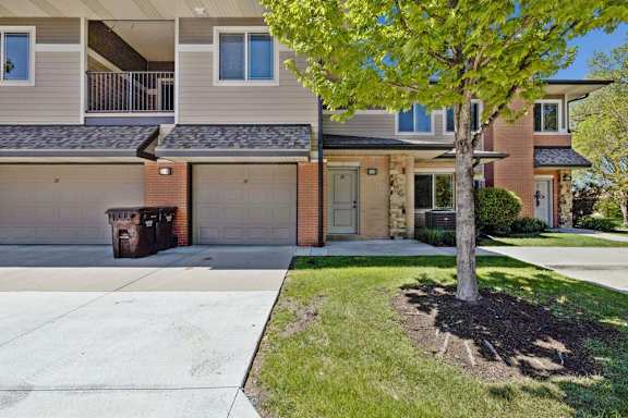 Apartment community exterior with attached garages, balconies, brick accents, and landscaped lawn.