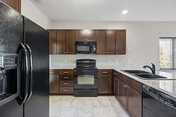 Kitchen with black refrigerator, oven, microwave, dishwasher, dark cabinetry, and light tile flooring.