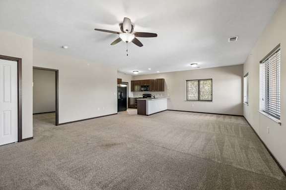 Open apartment living room with carpet, ceiling fan, fireplace, and kitchen with breakfast bar and dark cabinets.