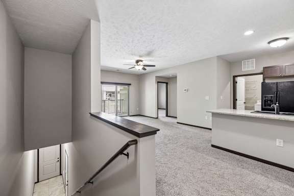 Open apartment living area with carpet, staircase railing, kitchen breakfast bar, and balcony door.