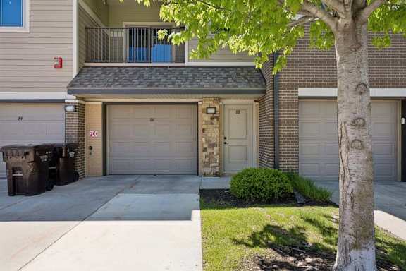 Apartment exterior with attached garage, front entry, balcony, brick accents, and landscaped lawn.