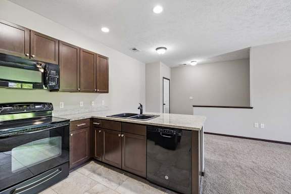 Apartment kitchen with dark cabinets, black appliances, speckled countertops, and tile flooring.