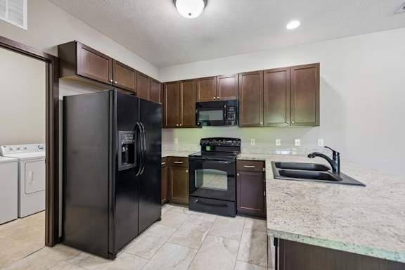 A kitchen with a black refrigerator and microwave, brown cabinets, and a marble countertop.