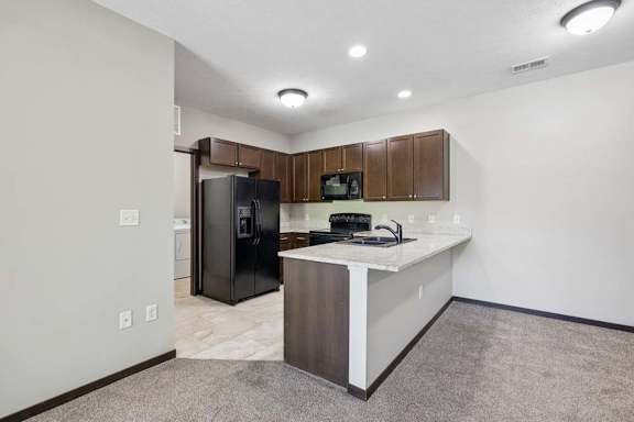 Open apartment kitchen with breakfast bar, dark cabinets, black appliances, and carpeted dining area.