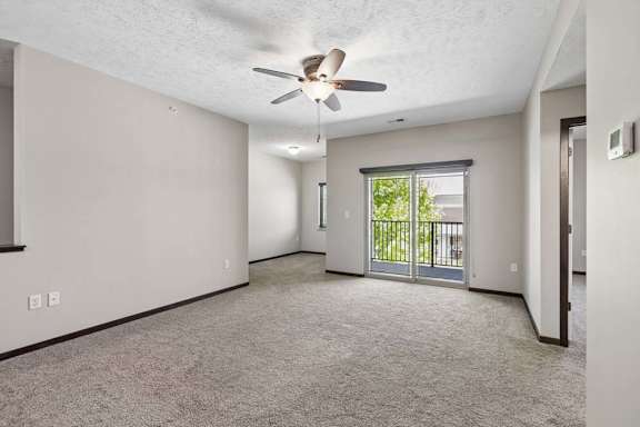 Open apartment living area with carpet, staircase railing, kitchen breakfast bar, and balcony door.