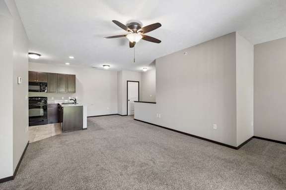 A spacious living room with a ceiling fan and a kitchen area in the background.